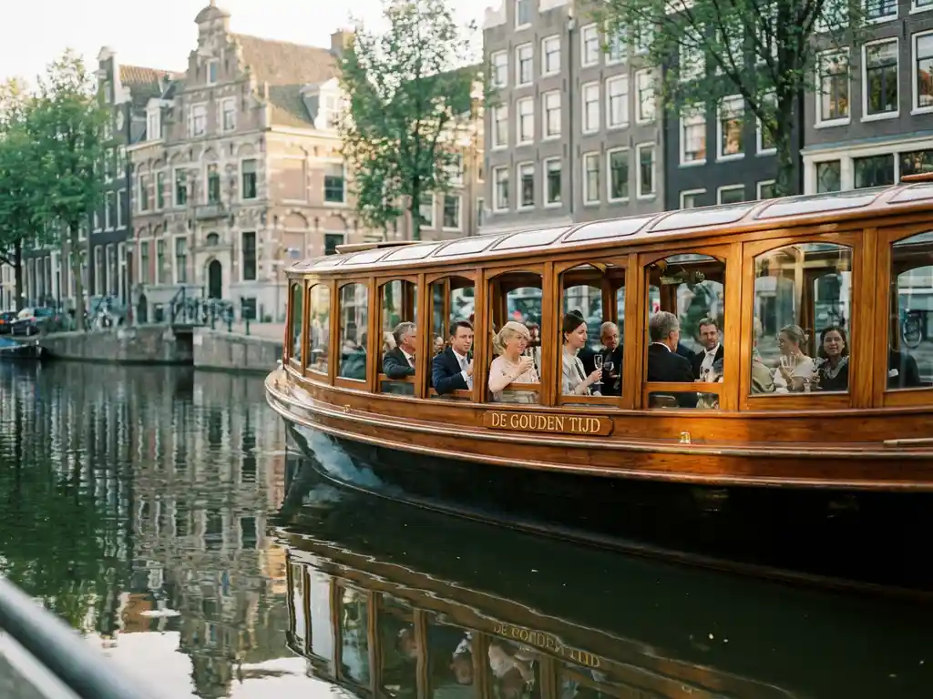 Klassieke overdekte Nederlandse salonboot uit 1910 vaart door smalle Amsterdamse gracht met gasten aan boord