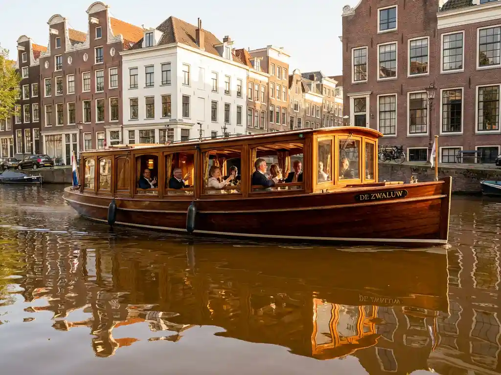 Klassieke overdekte tjalk uit 1910 vaart door Amsterdamse grachten met 17e-eeuwse grachtenpanden op de achtergrond