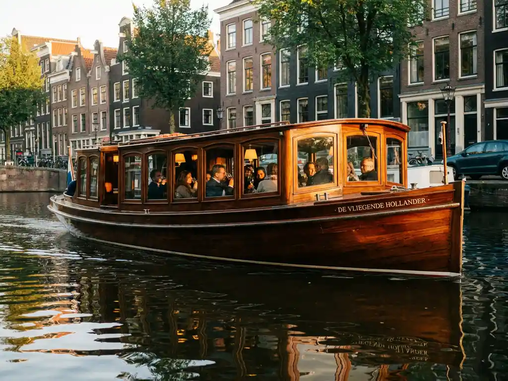 Historische gedekte salon tjalk uit 1910 vaart door Amsterdamse grachten, gepolijst irokohout glanst in goudkleurig avondlicht.